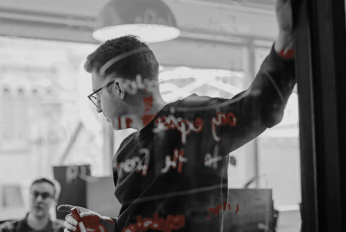 An engineer writing on a glass wall while a colleague looks on